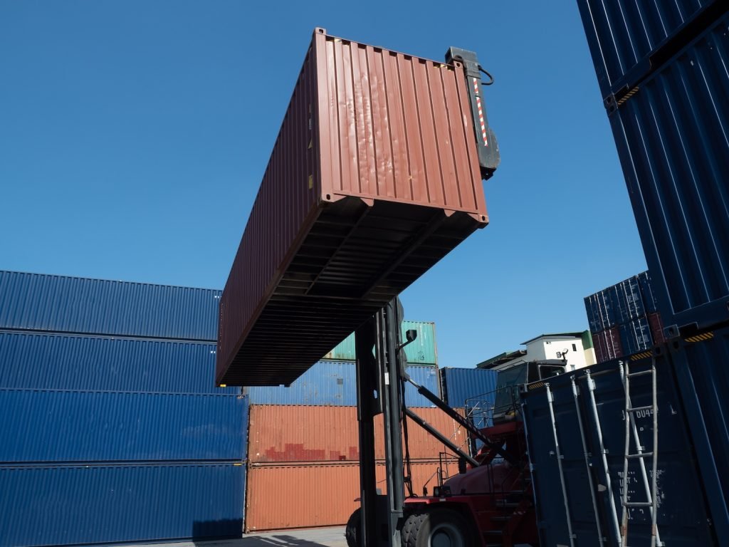 Forklift lifting a cargo container, demonstrating the difference between FCL (Full Container Load) and LCL (Less than Container Load) shipping options offered by SLG Logistics.