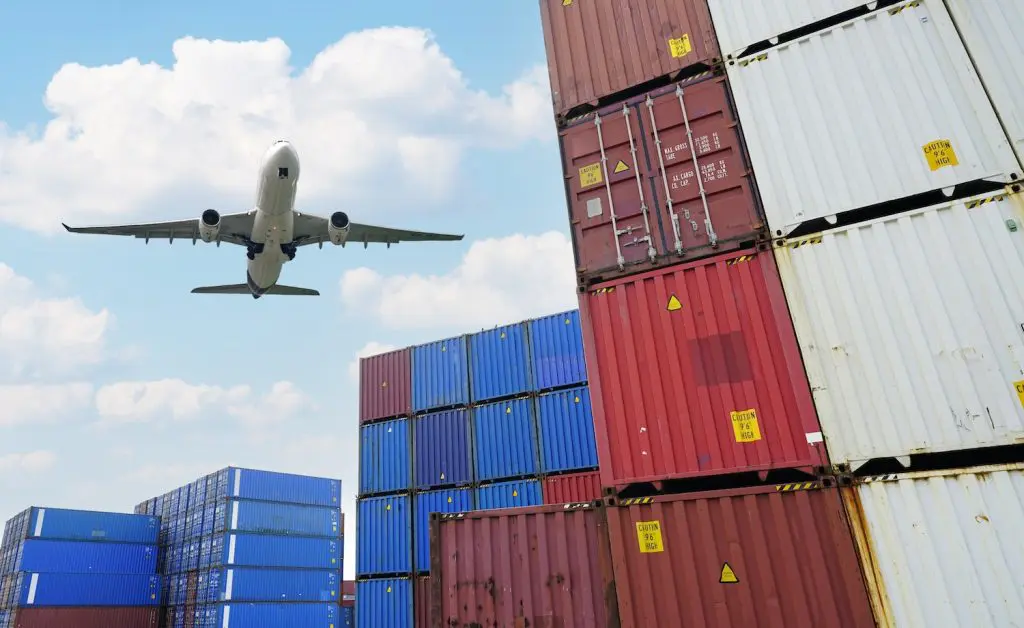 An aeroplane with air freight onboard flying over a dock of containers that will be sent by sea freight. The senders considered how to choose a reliable freight forwarder before partnering with SLG Logistics.