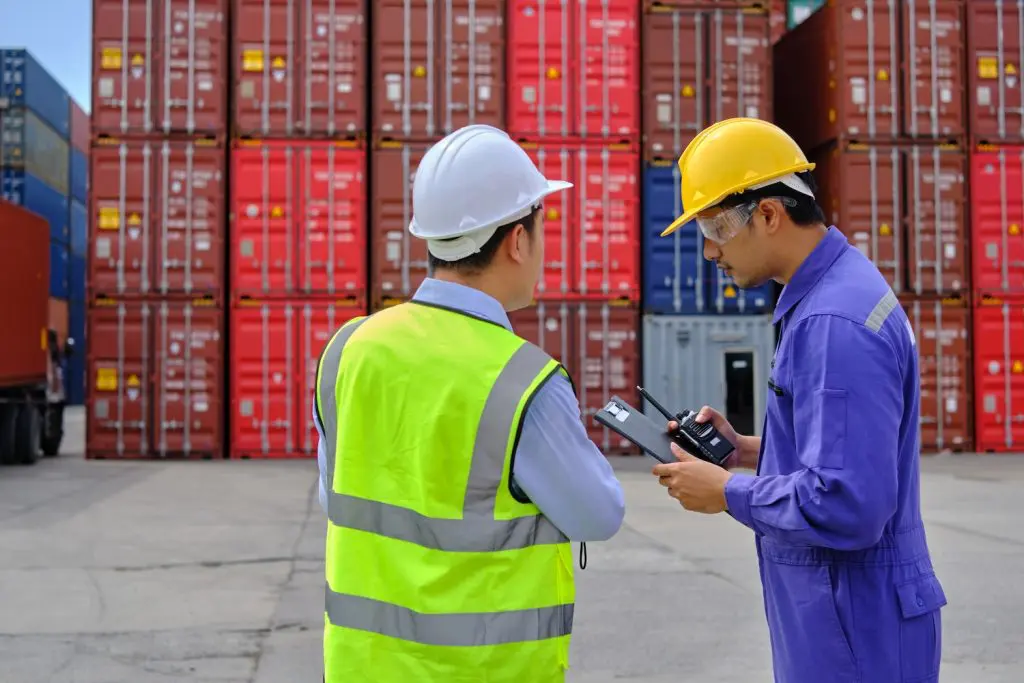 Two men discussing logistics in front of stacked containers, illustrating the importance of understanding the Philippines' import regulations for smooth trade